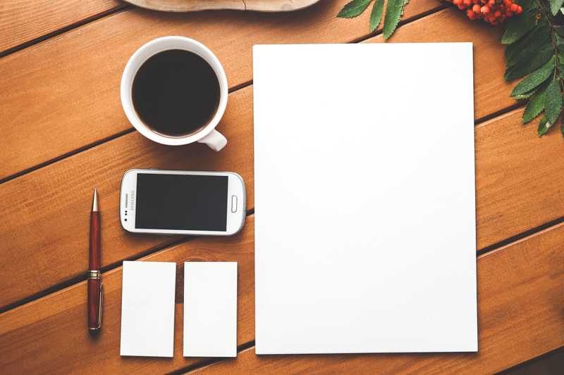 Cup of coffee, phone, pen, two cards, and a sheet of paper on a table